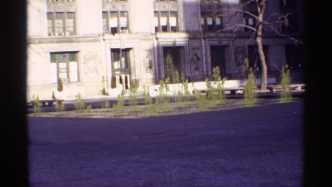 Small fountain jets in a paved plaza before an ornate multi-window building.