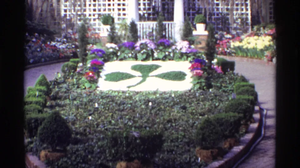 Visitor-shot 1968 Chicago garden view showing shaped plantings, flower beds, walkways, and downtown building facades.