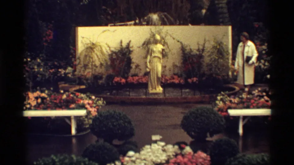 1968 Chicago garden frame showing a classical statue, planted beds, benches, shrubs, and a woman standing nearby.