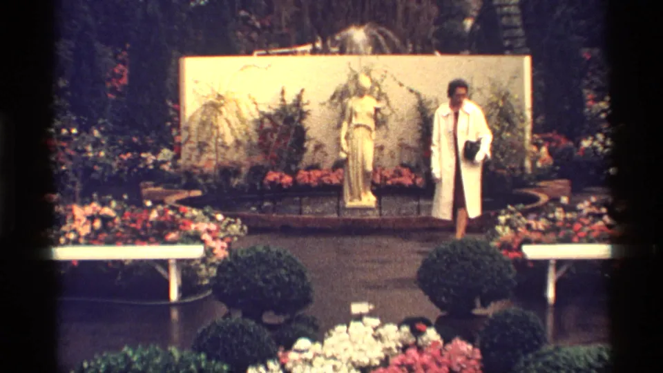The woman pauses near the right side of a 1968 Chicago garden display with a statue, flowers, shrubs, and white benches.