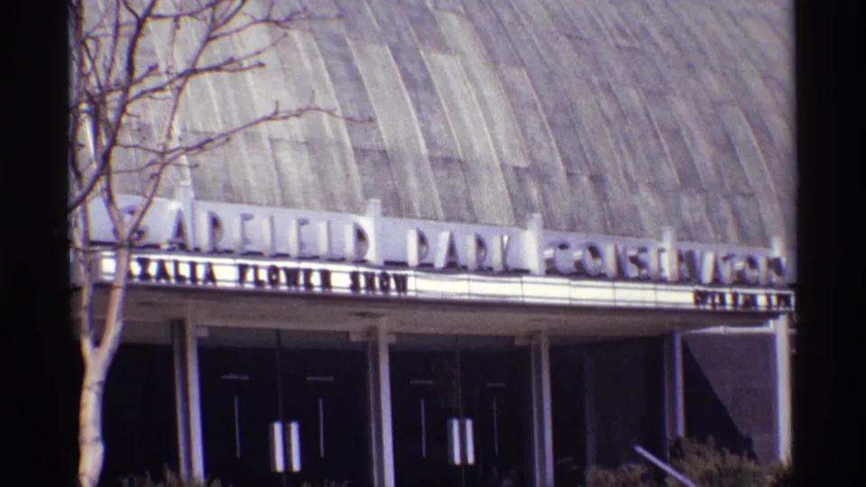 Handheld 8mm view of the Garfield Park Conservatory entrance, with large marquee lettering across the facade and dark double doors below.