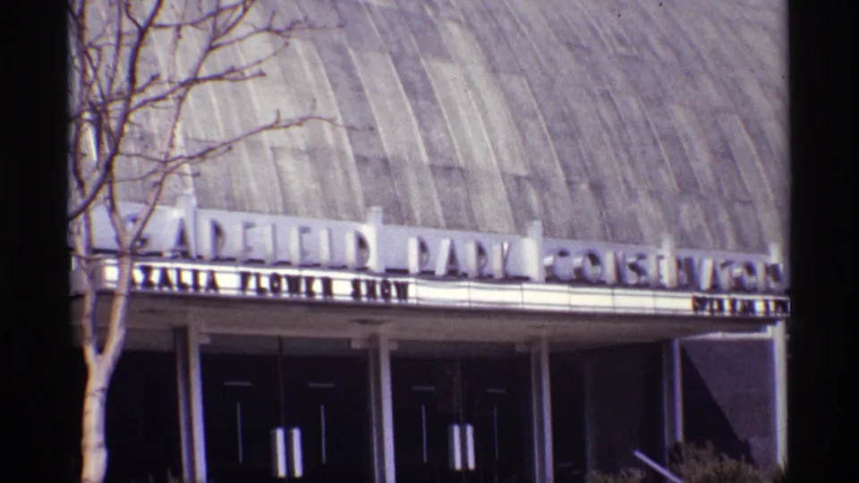 Exterior Chicago landmark view showing the Garfield Park Conservatory sign, curved roof surface, entrance doors, and a leafless tree in front.