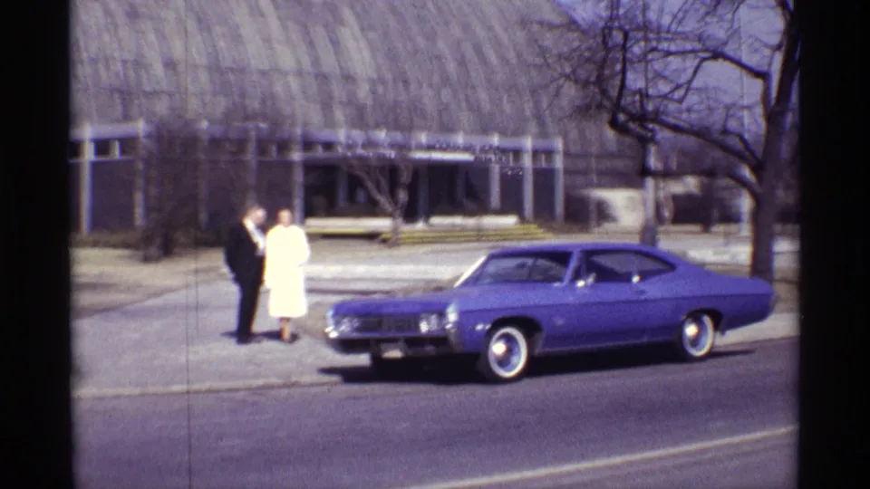 The couple remains near the purple car outside the Chicago conservatory, with the arched roof and bare trees visible.