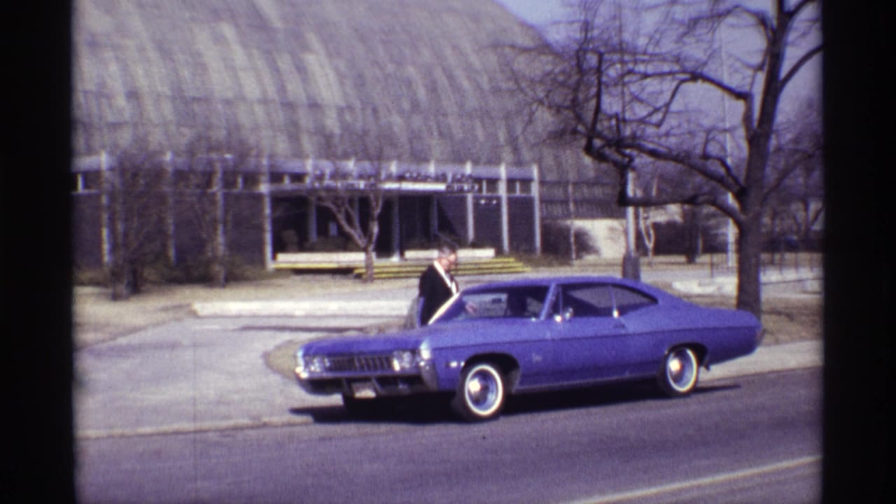 1968 Chicago home-movie frame showing a suited man beside a purple classic American car near a modernist building.