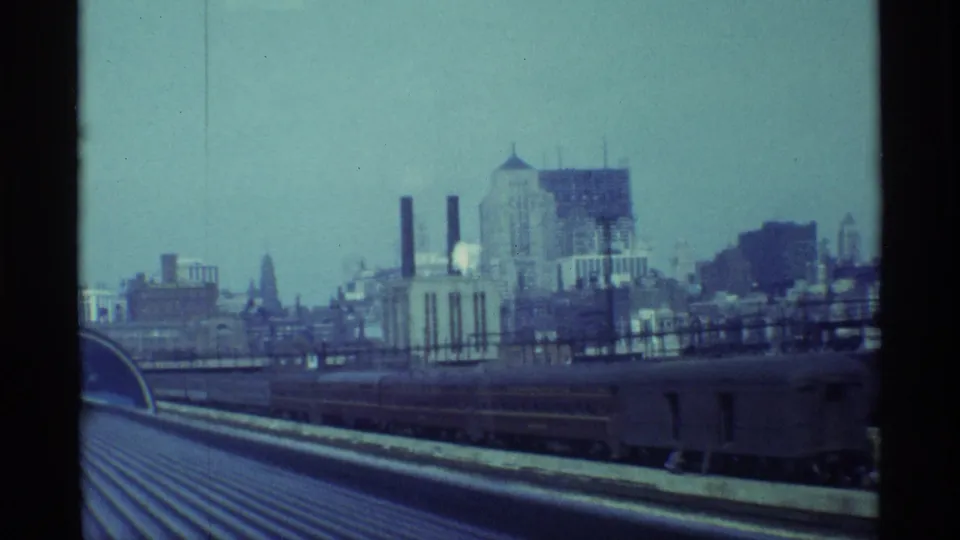 Chicago rail-side cityscape with industrial rooftops, smokestacks, and a train car seen from an elevated vantage point.