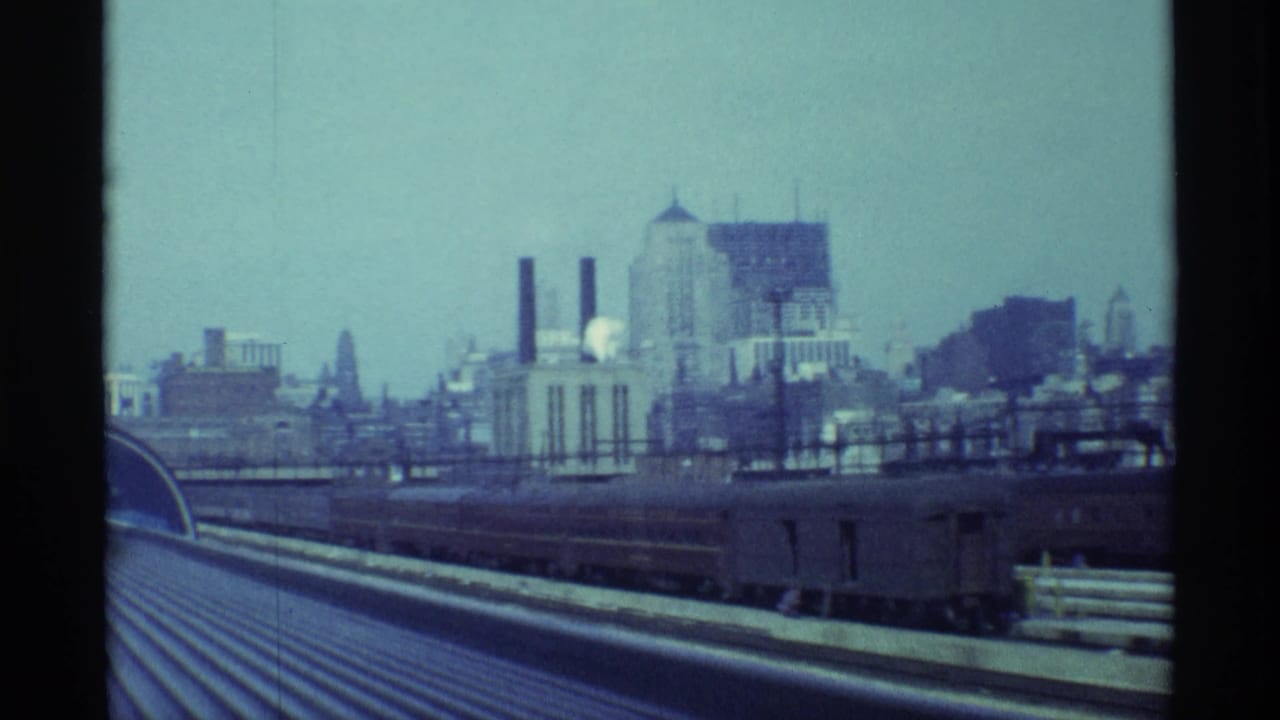 1968 Chicago train-top view showing corrugated rail roof, adjacent tracks, industrial buildings, smokestacks, and distant high-rises.