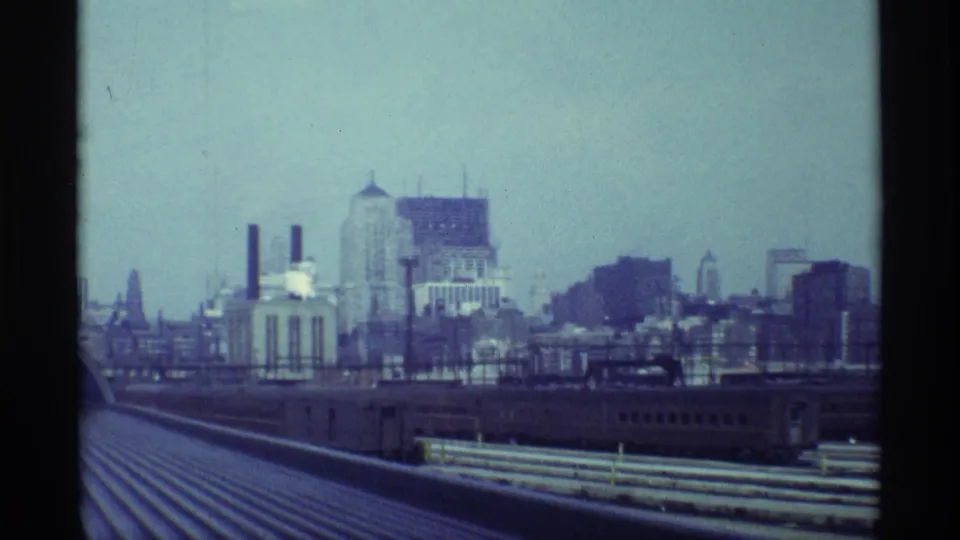 1968 Chicago home-movie frame from a moving train, with roof lines, adjacent rail equipment, industrial buildings, and skyline under hazy light.