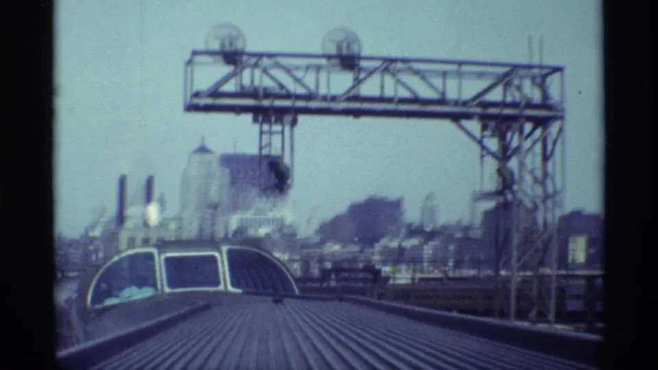 1968 Chicago train-view frame with a metal gantry structure above the rail line and industrial skyline in the distance.