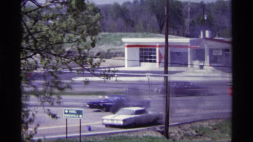 1968 Chicago roadside scene with a white car emitting black smoke as other 1960s cars pass on the road.