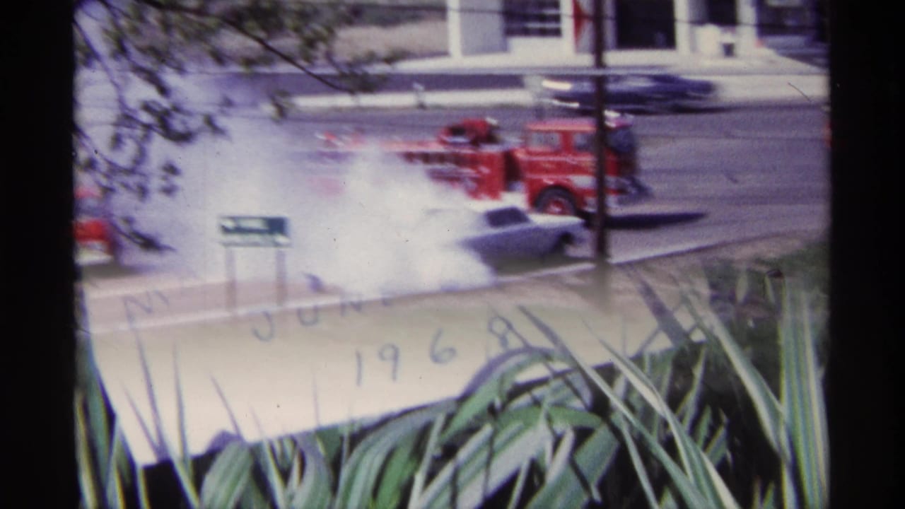 Red fire truck beside heavy white smoke near a white car on a street.