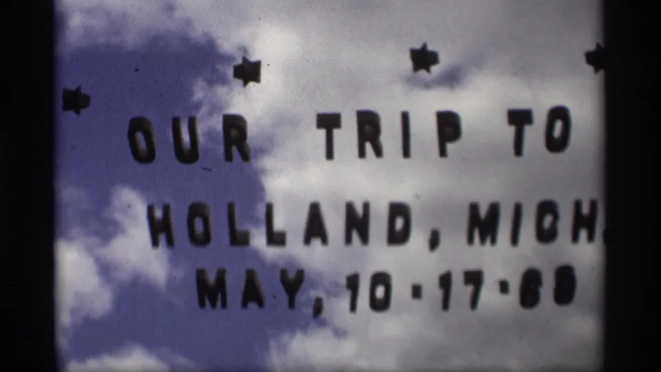1969 8mm vacation title card for Holland, Michigan, with black letters over a cloudy sky and small star decorations.