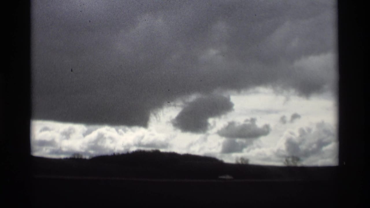 Dark horizon beneath heavy gray clouds seen through a moving frame.