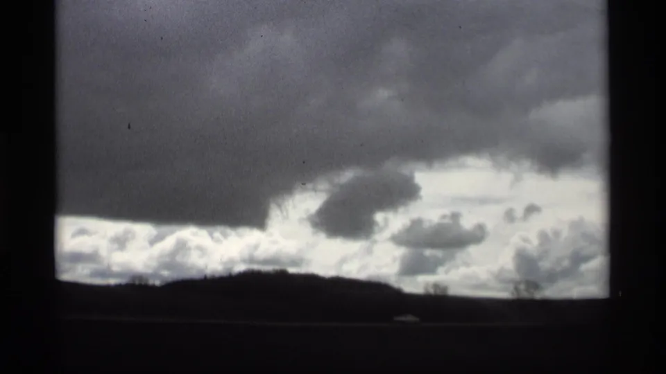 1969 Holland, Michigan 8mm view of heavy overcast clouds above a dark roadside horizon from a moving vehicle.