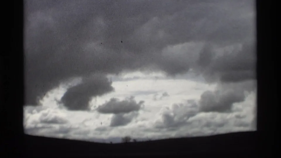 Holland, Michigan home-movie frame with layered overcast clouds, a bright sky gap, and a dark low horizon.