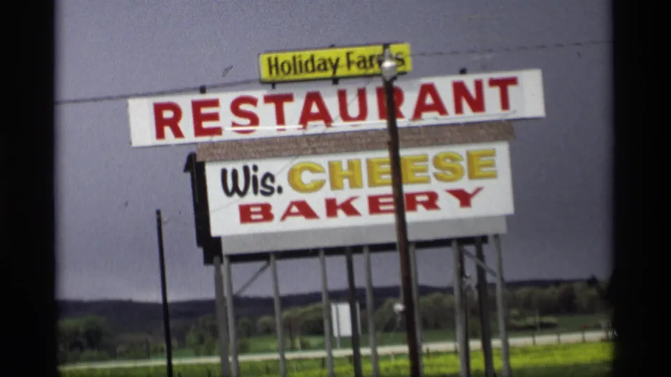 Roadside Holiday Farms Restaurant sign with Wis. Cheese Bakery lettering in a 1969 Holland, Michigan home-movie frame.