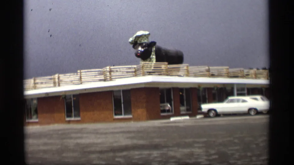 1969 Holland, Michigan motel exterior showing the large roof animal chef figure above a brick building and parked station wagon.