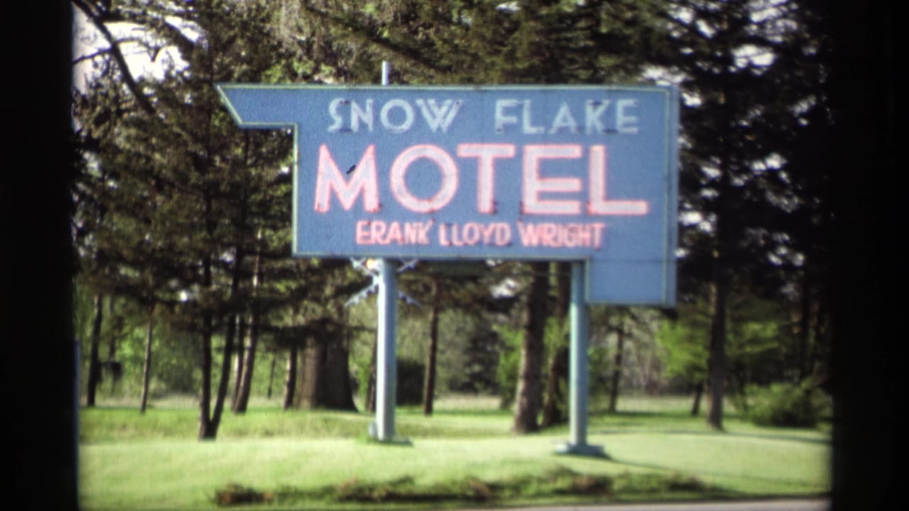Blue Snow Flake Motel sign beside grass and evergreen trees.