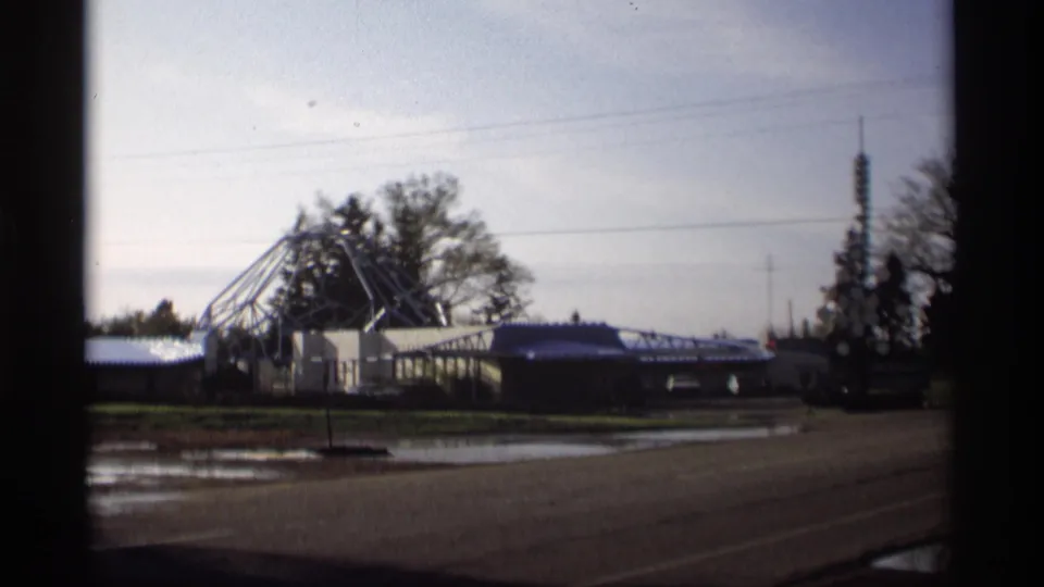 Wide 1969 roadside frame in Holland, Michigan with an angular roof structure, low motel buildings, trees, wires, and wet pavement.