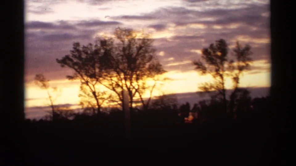 Holland, Michigan dawn or sunset scene with silhouetted trees, a dark foreground, and warm cloud bands on 8mm film.