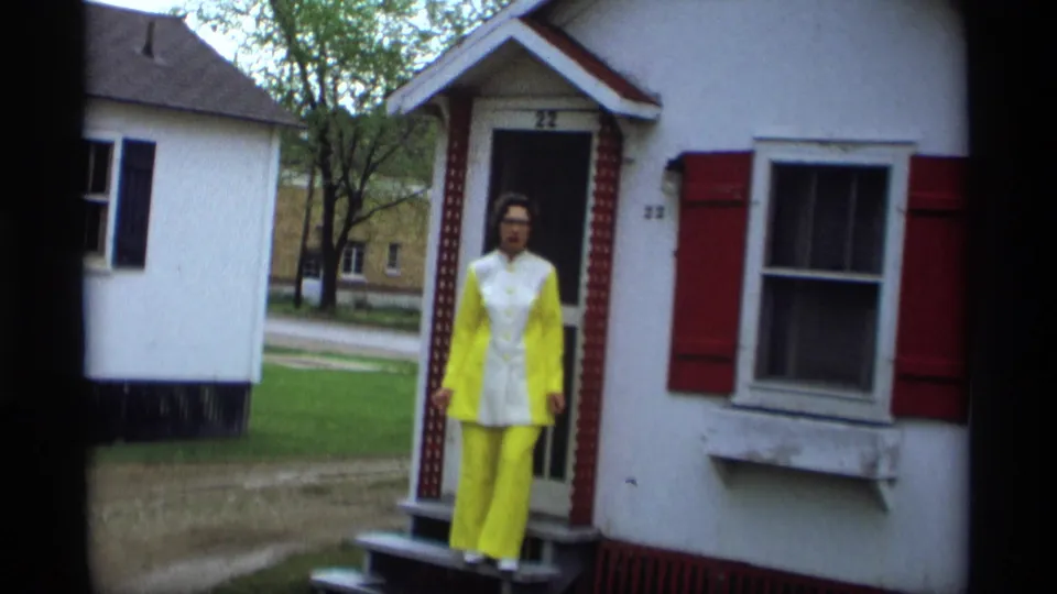 In Holland, Michigan, 1969, a woman in a bright yellow and white suit poses at the doorway of a small white house.