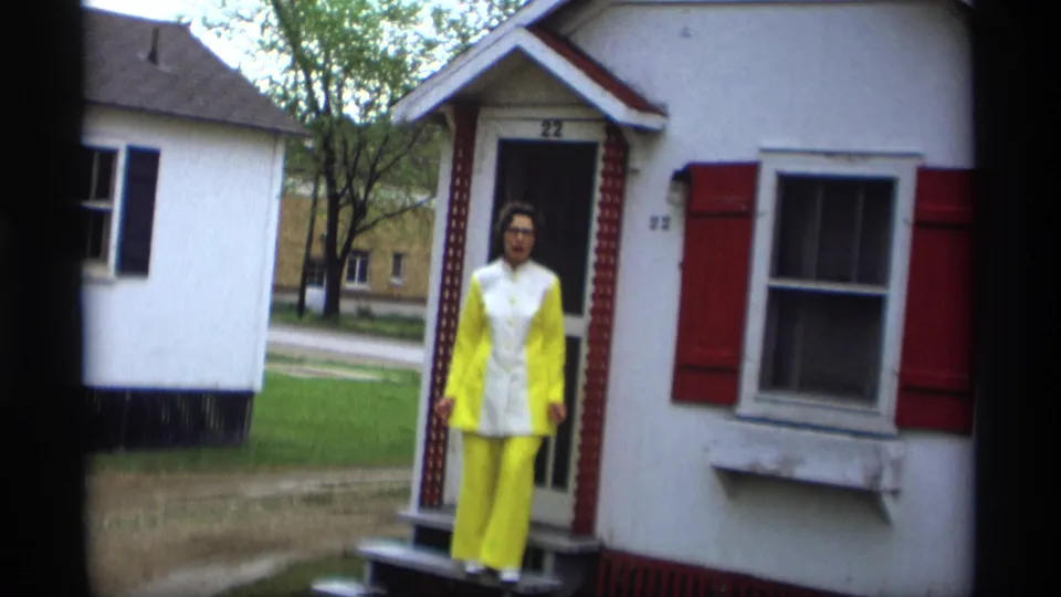 The woman remains on the porch of the Holland, Michigan house, framed by the doorway, red shutters, and lawn beyond.