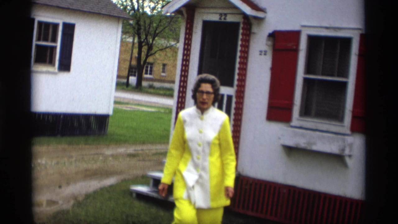 In 1969 Holland, Michigan footage, a woman walks toward the camera past a white house with red shutters and house number 22.