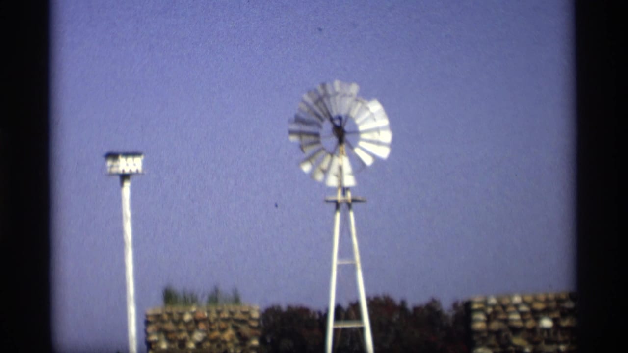 White windmill and pole-mounted birdhouse against a blue sky with stonework below.