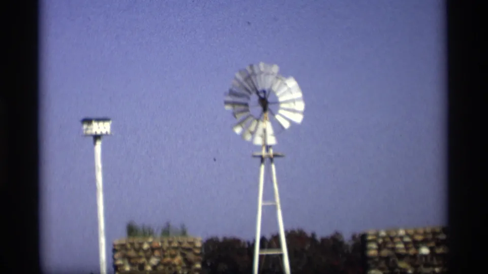 1969 Holland, Michigan 8mm frame showing a white windmill, tall birdhouse pole, stacked stonework, trees, and blue sky.