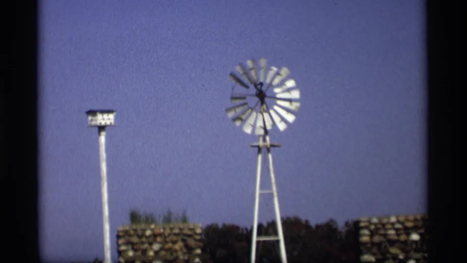 1969 Holland, Michigan 8mm frame with a white windmill, pole-mounted birdhouse, stacked stonework, trees, and visible film grain.