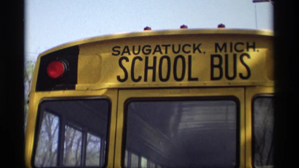 Close view of the rear of a yellow school bus marked Saugatuck, Mich., with windows and a red signal light visible.