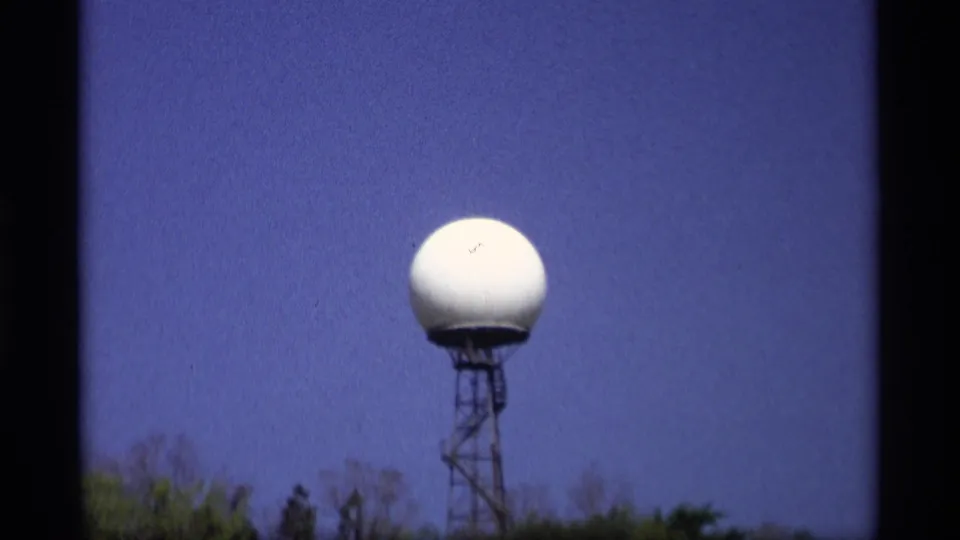 1969 Holland, Michigan frame showing a white dome on a tower, with blue sky and low treetops below.