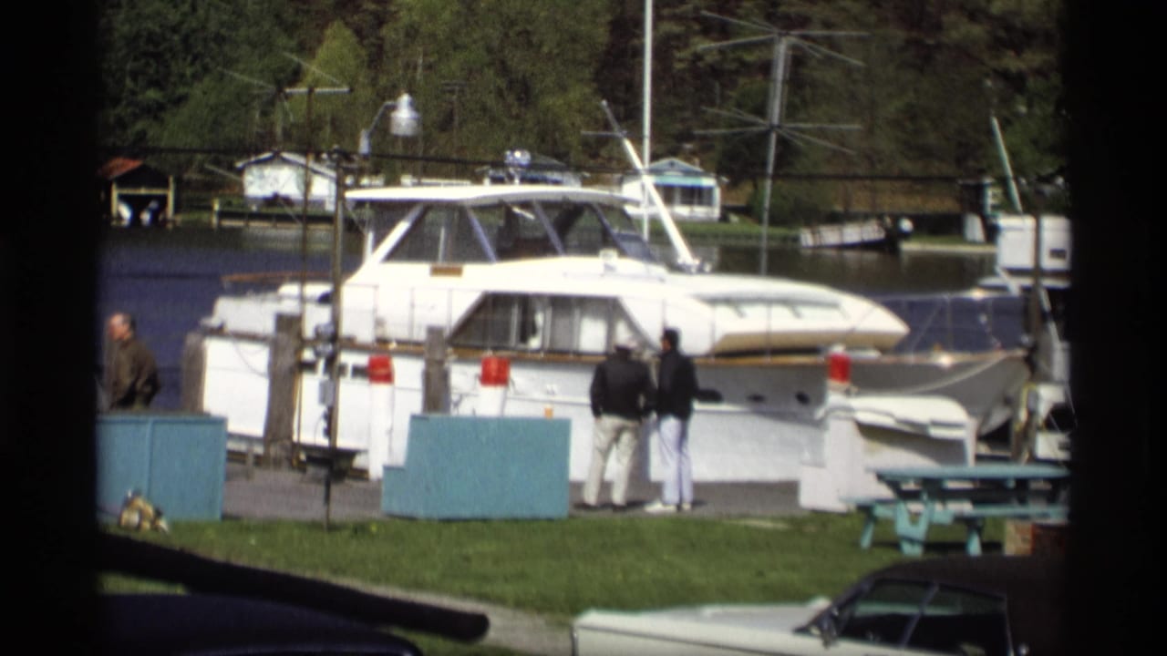 White motor yacht docked at a marina with adults standing nearby and water behind it.