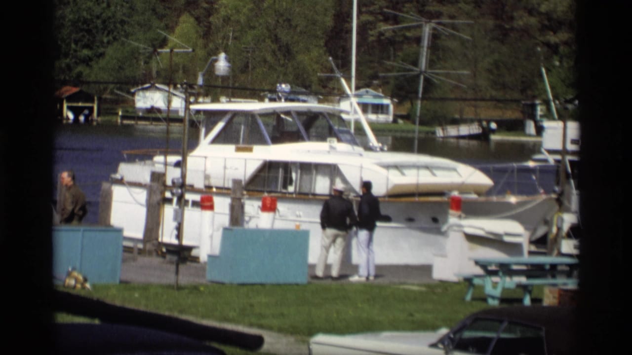 Docked yacht beside a grassy marina area with adults standing near the pier.
