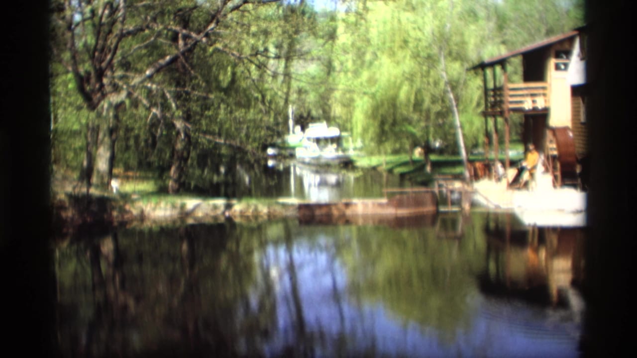 Calm river bordered by trees with a waterside house, dock, and small boat.