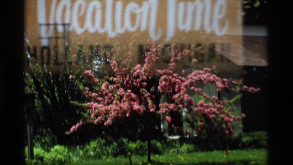 Holland, Michigan home-movie frame with a pink flowering shrub and lawn, partly overlaid by the title card exposure.