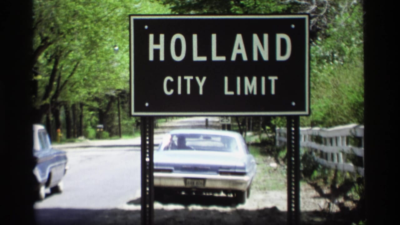 1969 Holland, Michigan home-movie frame showing a city-limit sign, roadside trees, and large American cars.
