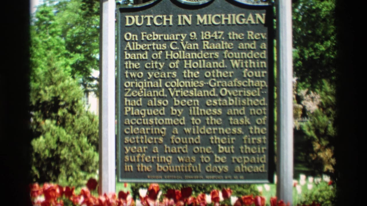 The Dutch in Michigan marker fills the frame, with readable gold text, red tulips below, and leafy trees behind it.