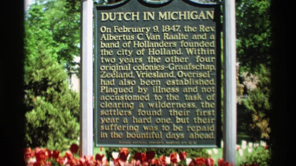 The Dutch in Michigan marker fills the frame, with readable gold text, red tulips below, and leafy trees behind it.