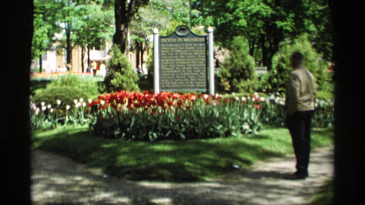 Man standing near a Dutch in Michigan marker surrounded by red and white tulips in a shaded park.