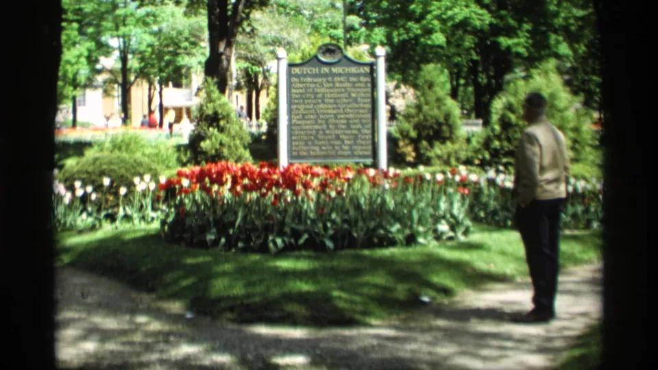 Holland, Michigan park scene from 1969 with a Dutch history marker, bright tulips, shaded trees, and a visitor at right.