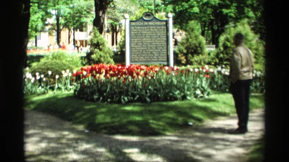 1969 home-movie view in Holland, Michigan with a visitor facing the Dutch in Michigan marker amid manicured tulip beds.