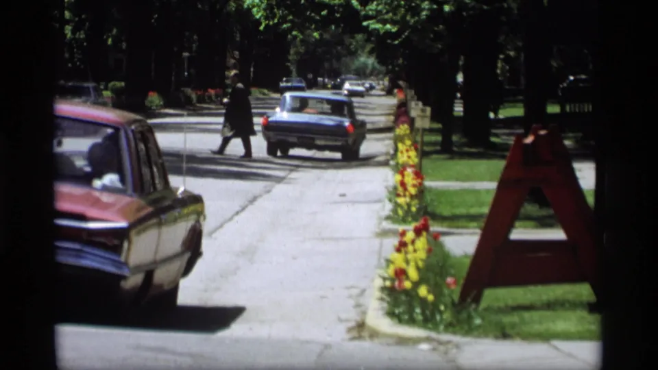 The Holland, Michigan street view shows vintage cars, pedestrians, flower beds, and a large letter A sign near the curb in 1969 footage.