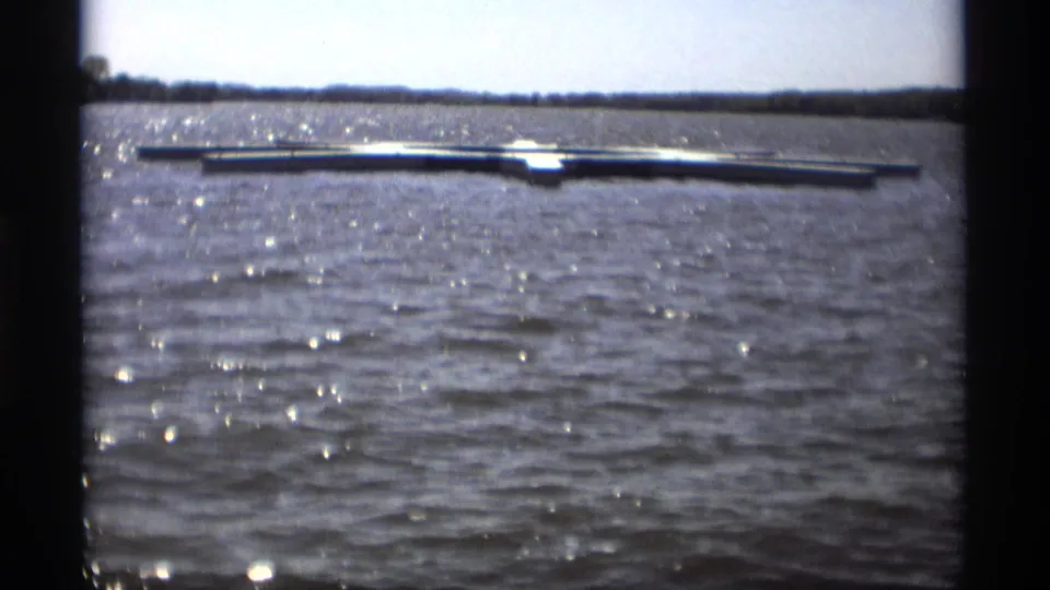 1969 Holland, Michigan lake scene with sunlit ripples and a long floating dock seen from a handheld 8mm camera.