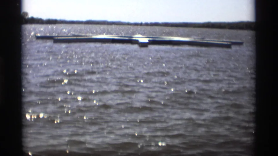 A 1969 8mm view in Holland, Michigan shows a floating dock across rippled lake water with bright sun glints.