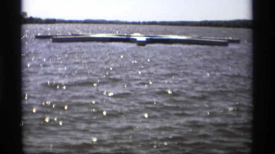 The 1969 Holland, Michigan lake footage holds on a floating dock and shimmering water in a soft 8mm home-movie frame.