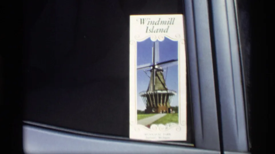 A Windmill Island brochure with a windmill photograph is shown inside a car, linking the home-movie visit to Holland, Michigan tourism.