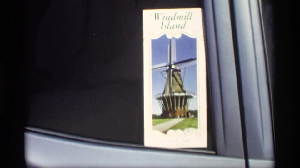 1969 Holland, Michigan home-movie frame showing a Windmill Island brochure with a windmill picture near a vehicle window.
