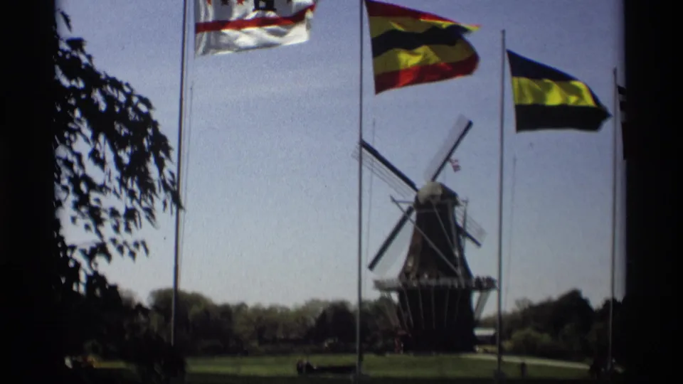 Wide 1969 Holland, Michigan park view of the Windmill Island windmill behind international flags and a grassy foreground.