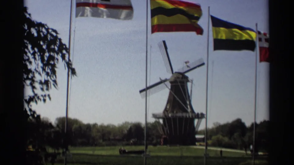 Holland, Michigan home-movie view of the Windmill Island windmill, flagpoles, lawn, trees, and distant visitors.