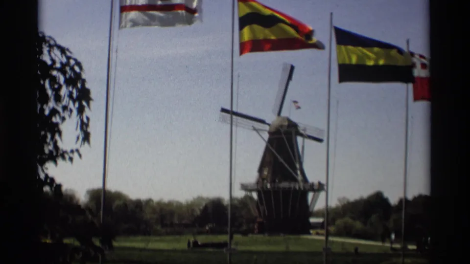 Final 1969 Holland, Michigan frame with the Windmill Island windmill partly framed by flags, lawn, trees, and distant people.